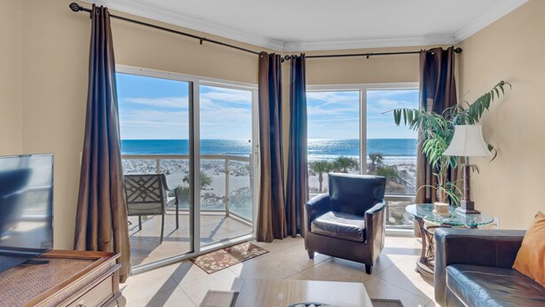 Un salon équipé d’un téléviseur, d’un canapé, d’un fauteuil, d’une table et offrant une vue sur la plage grâce à de grandes fenêtres.
