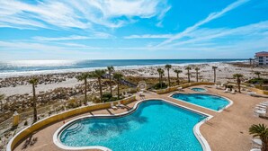 Un espace piscine comprenant deux piscines, une vue sur la plage et un bâtiment en arrière-plan.