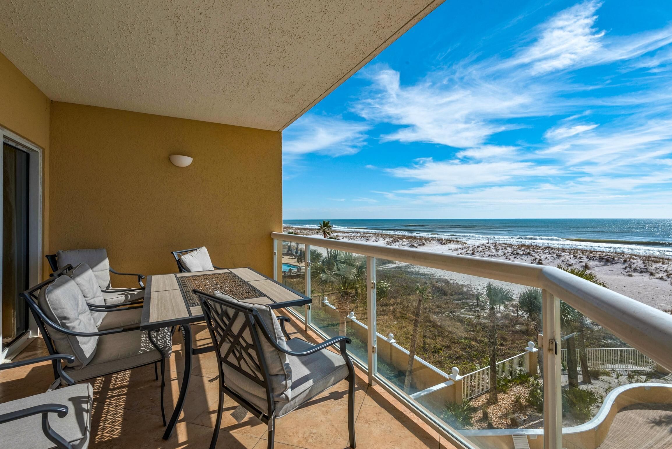 Un balcon avec une table et des chaises, donnant sur une plage sous un ciel dégagé.