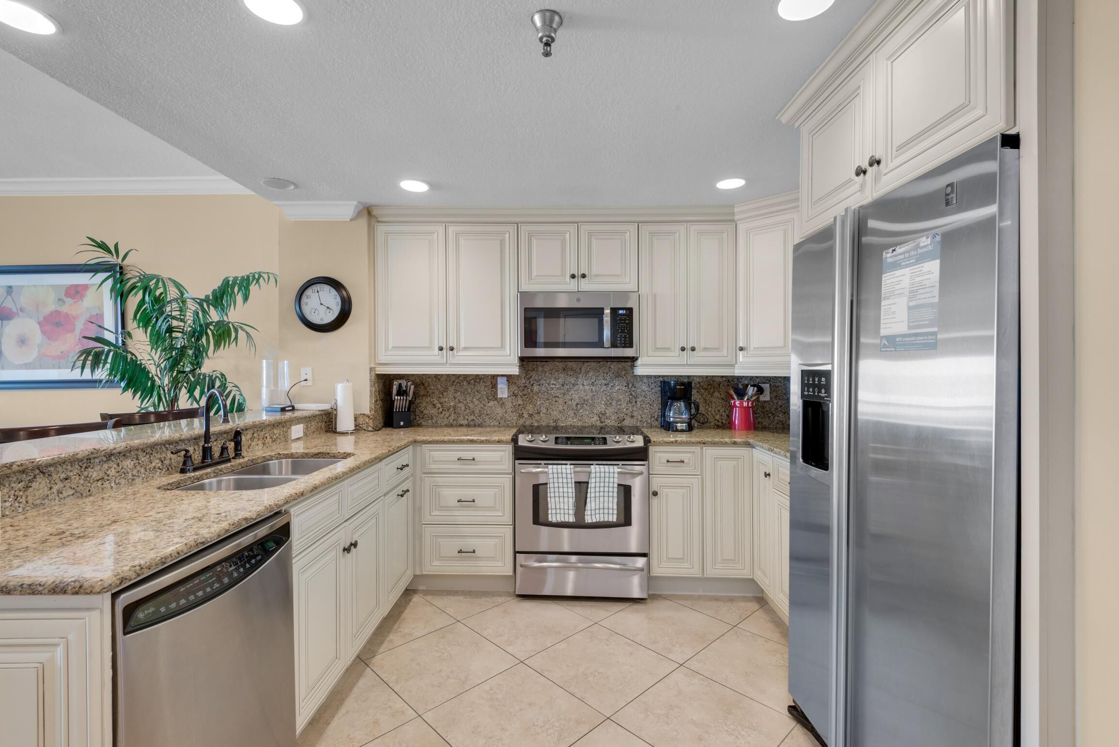 A kitchen with white cabinets, stainless steel appliances, a granite countertop, and a clock on the wall.