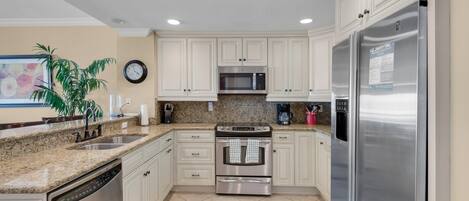 A kitchen with white cabinets, stainless steel appliances, a granite countertop, and a clock on the wall.