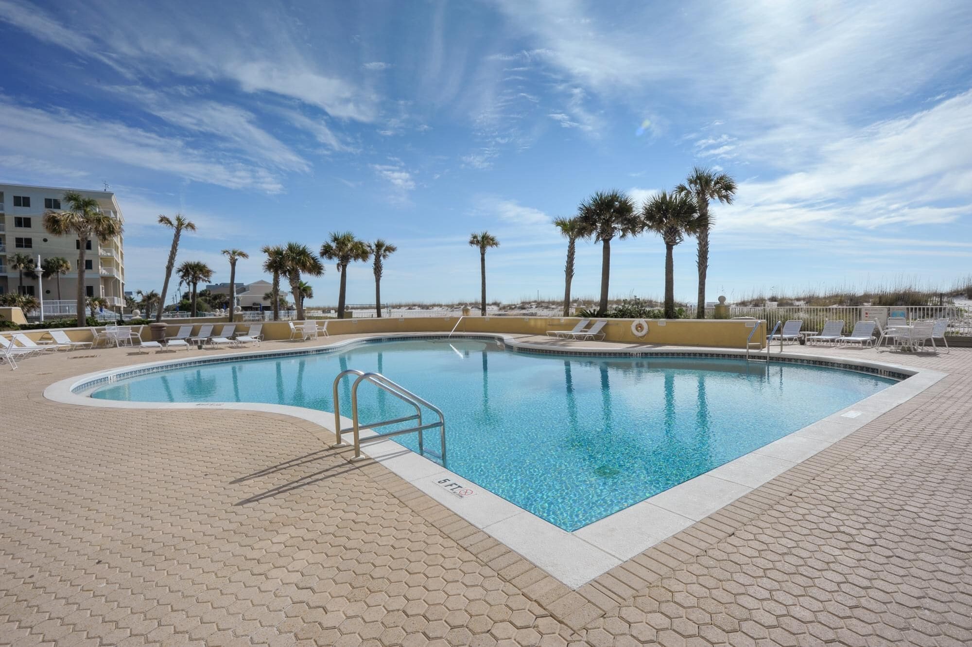 A swimming pool with lounge chairs and palm trees, surrounded by a paved deck.