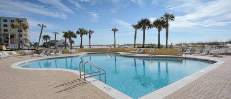 A swimming pool with lounge chairs and palm trees, surrounded by a paved deck.