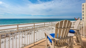 A beach view from a balcony with a railing, a wooden chair, and a table. - Seahorse Unit M (Pensacola Beach)