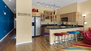 A modern kitchen with wooden cabinets, a stainless steel refrigerator, and a central island with bar stools. - Seahorse Unit M (Pensacola Beach)