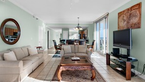 A spacious living room with a beige sofa, a wooden coffee table, and a television on a stand. - Emerald Dolphin Unit 510 (Pensacola Beach)