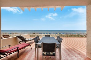 A terrace with a table and chairs, overlooking a beach and the sea. - Sans Souci Unit 104 (Pensacola Beach)
