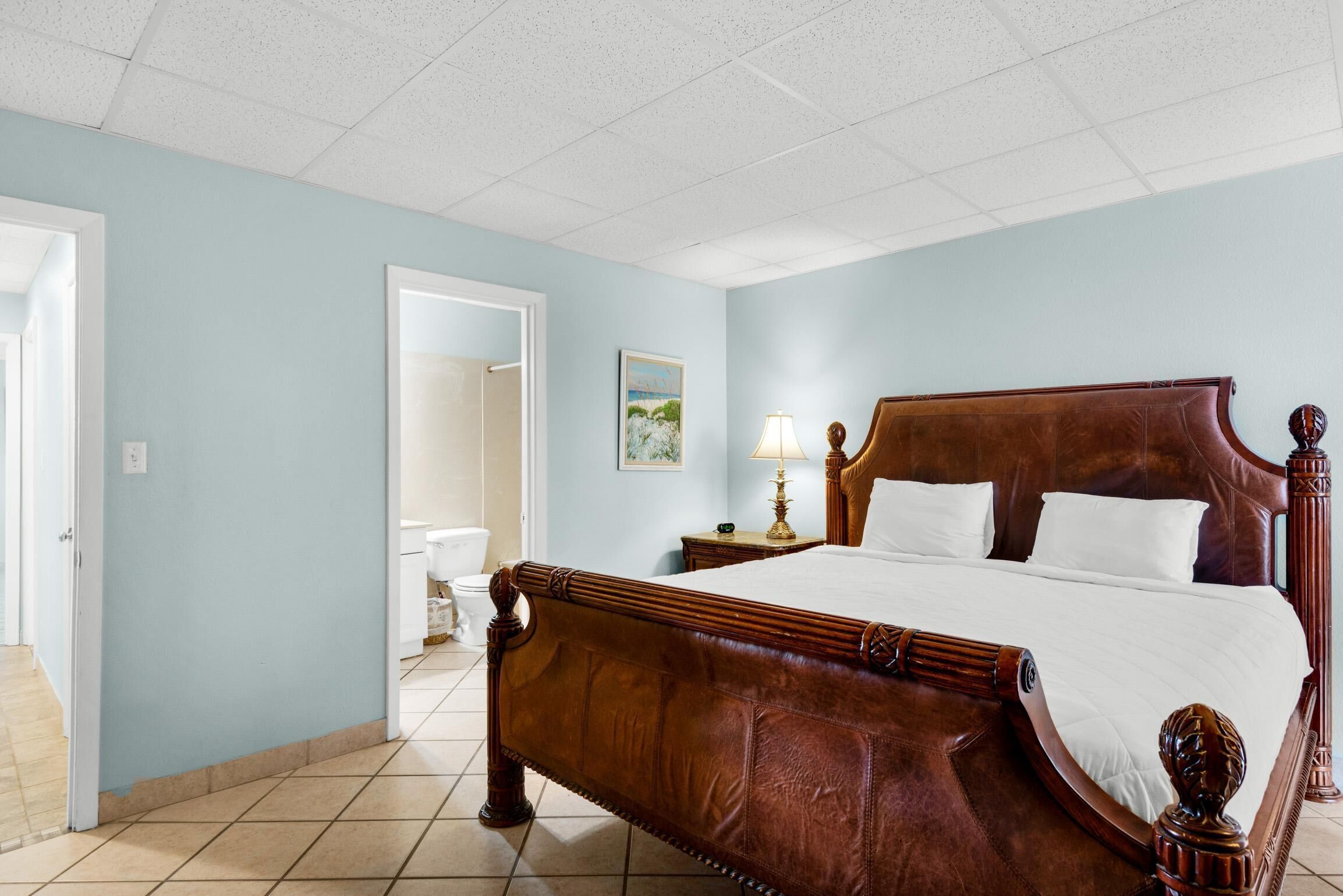 A spacious bedroom with a large wooden bed, a bedside table with a lamp, and a door leading to another room.