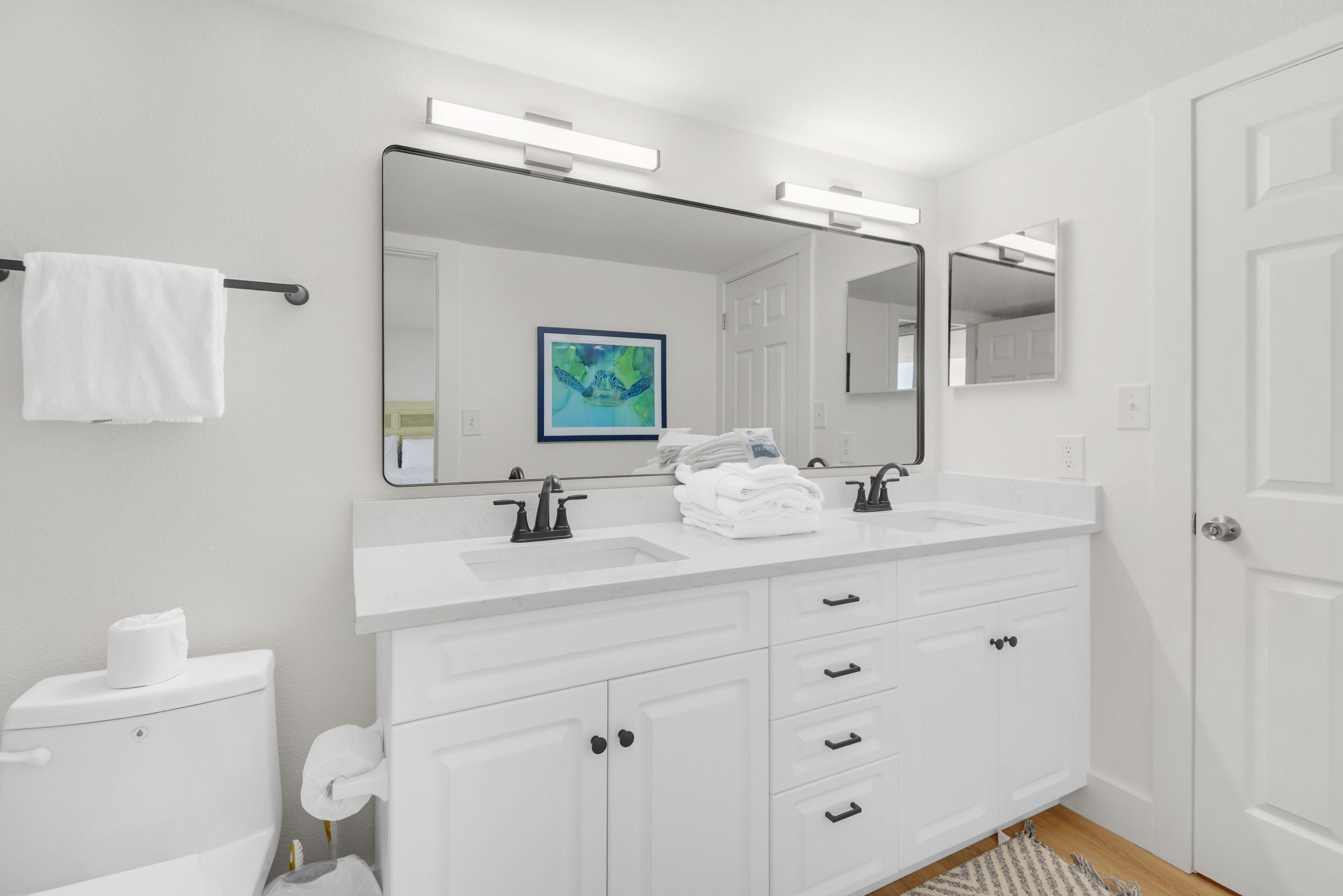 A modern bathroom with a white vanity, a large mirror, and a toilet.