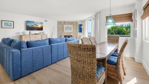 Ein modernes Wohnzimmer mit einem blauen Ecksofa, Korbstühlen, einem Holzesstisch und Kunstwerken an den Wänden.