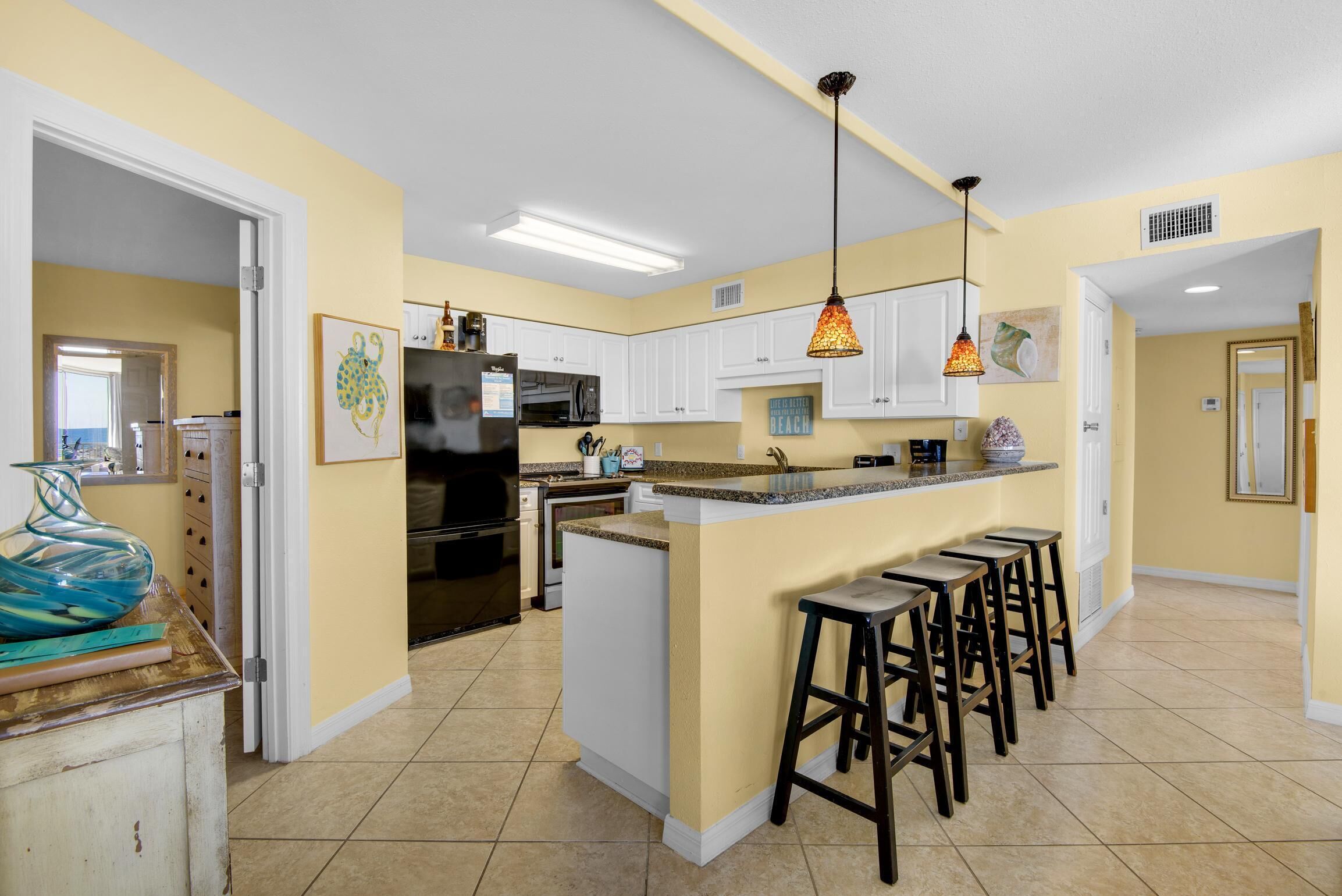 Una cocina con armarios blancos, una isla central con taburetes, un refrigerador y un microondas.