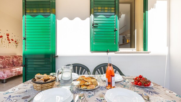 Una mesa de comedor dispuesta con platos, cubiertos, una botella de vino y una cesta de pan.