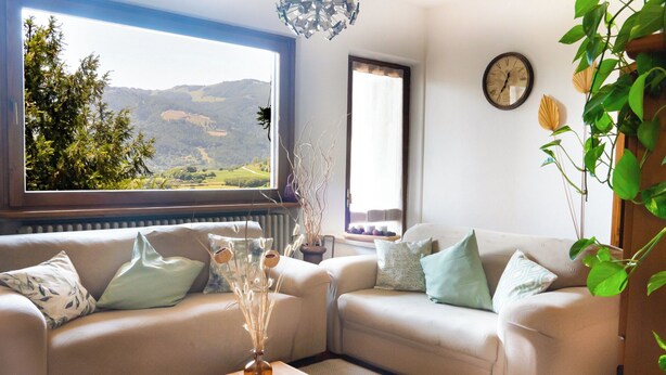 Un salon avec deux canapés, une table basse en bois, une vue sur un paysage par la fenêtre et une horloge murale.