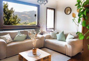 A living room with two sofas, a wooden coffee table, a view of a landscape through a window, and a wall clock.