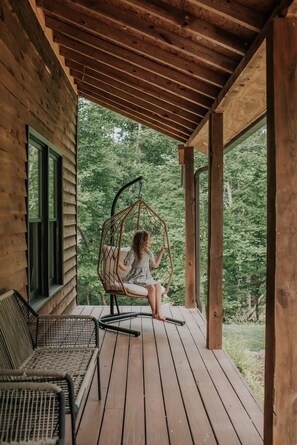 A wooden deck with a hanging chair and a wicker chair. - Wine Country Getaway Chalet  Pet Friendly (Dahlonega)