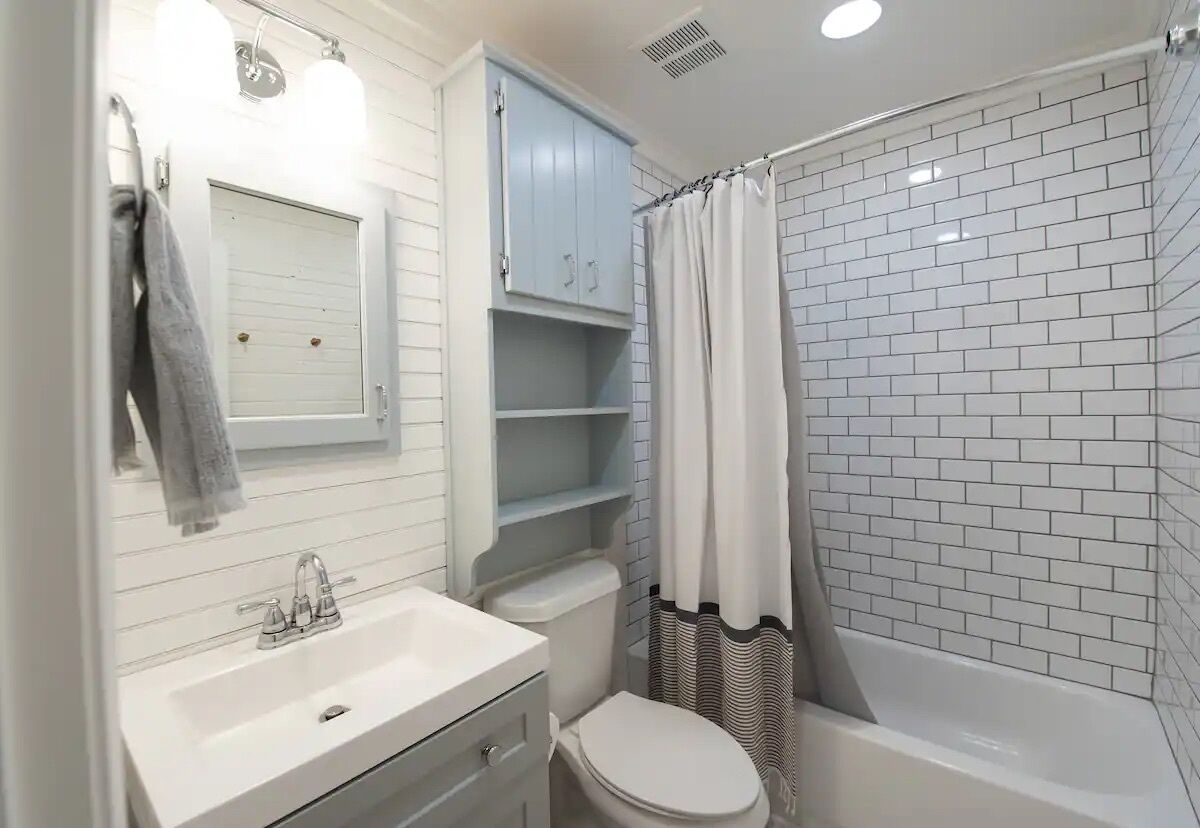 Un baño con un lavamanos blanco, un inodoro, una ducha con cortina a rayas y un armario azul claro.
