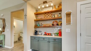 Une cuisine avec des meubles de rangement en bois, un plan de travail sur lequel sont disposés divers ustensiles de cuisine, et une étagère murale ornée d’objets décoratifs.