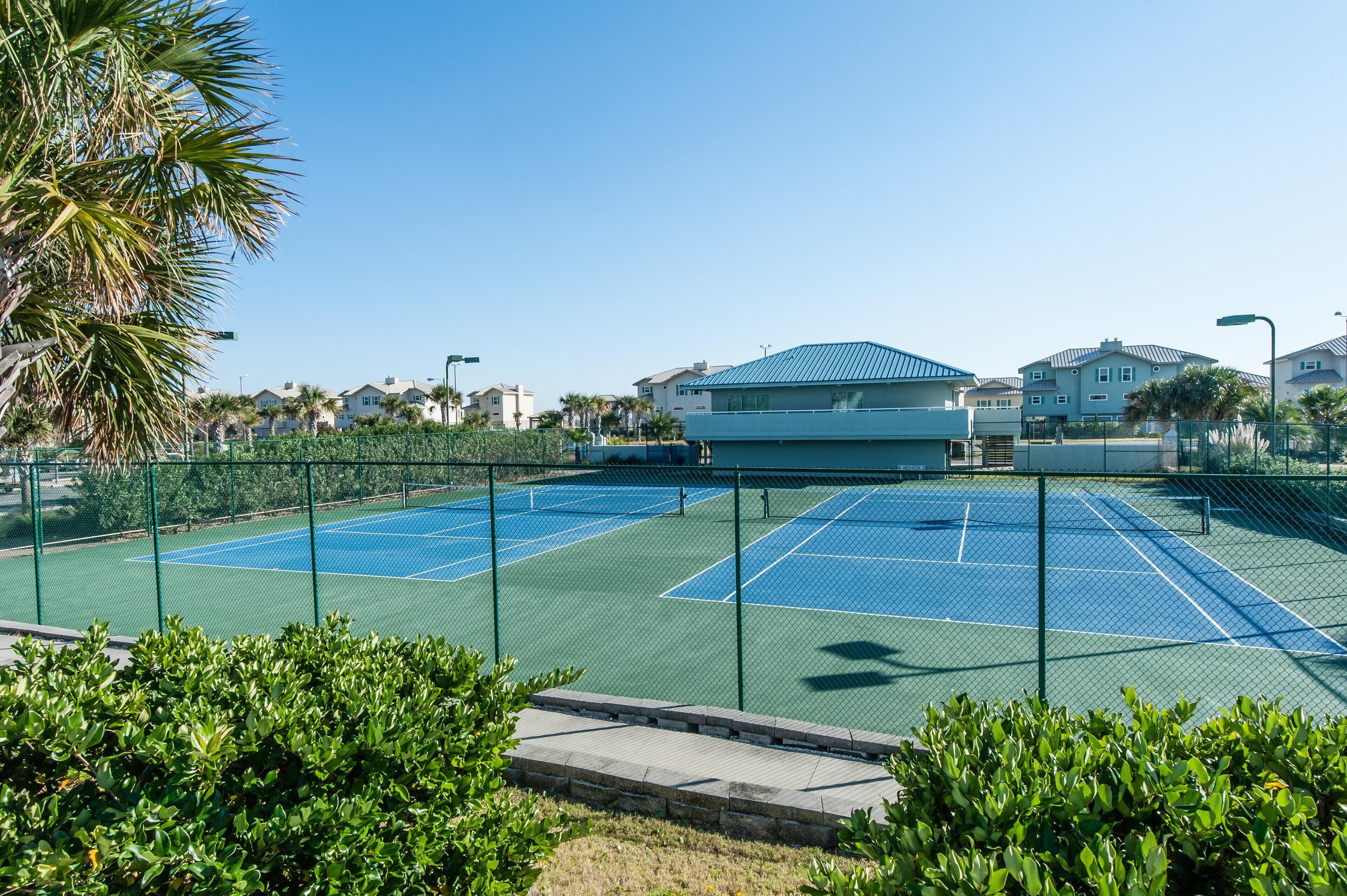 Un court de tennis entouré d’une clôture, avec un bâtiment en arrière-plan.