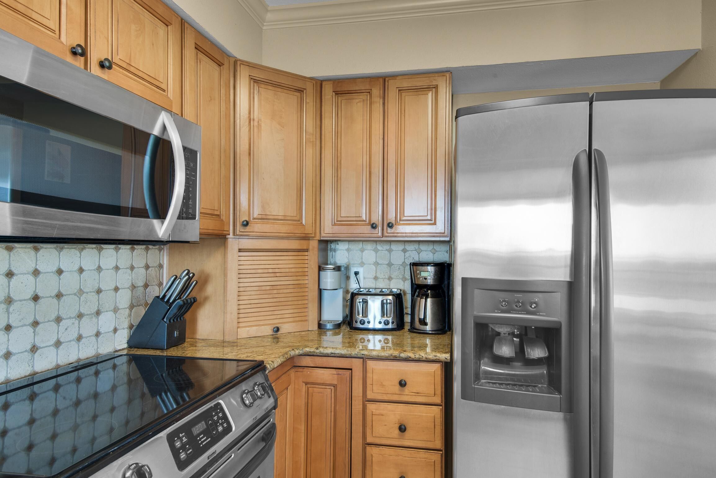 A kitchen with wooden cabinets, a stainless steel refrigerator, a microwave, a stove, and a coffee maker.