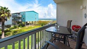 Un balcone con tavolo e sedie, vista su una spiaggia e un edificio blu.