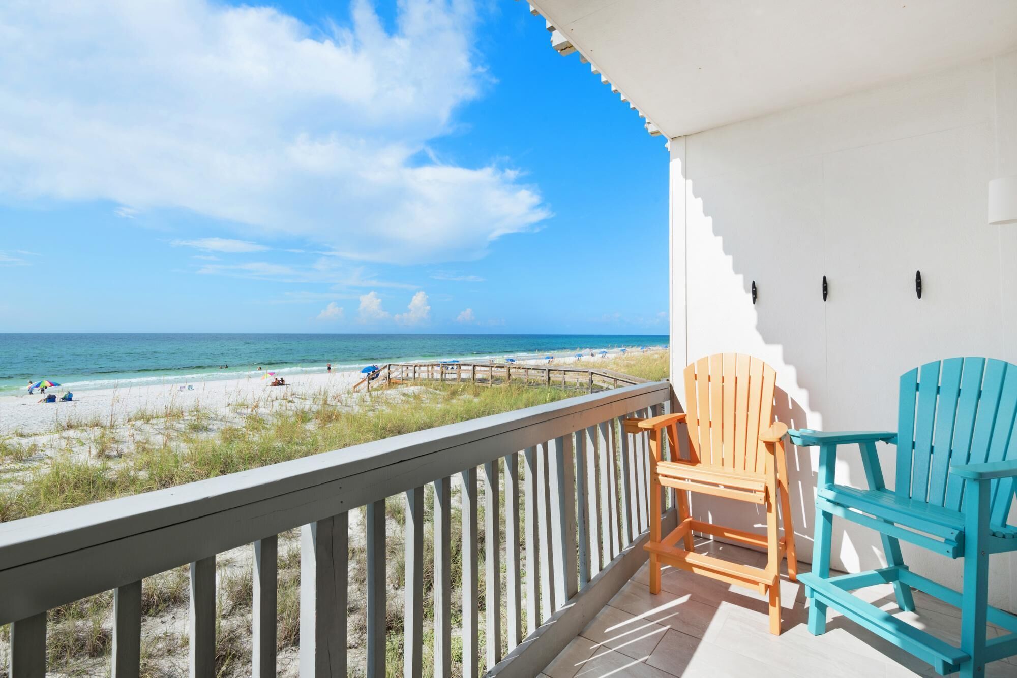 Ein Balkon mit Blick auf den Strand, Holzstühle und eine weiße Wand.