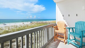 Een balkon met uitzicht op het strand, houten stoelen en een witte muur.