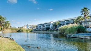 Een hotel aan het water met een zwembad, palmbomen en een steiger.