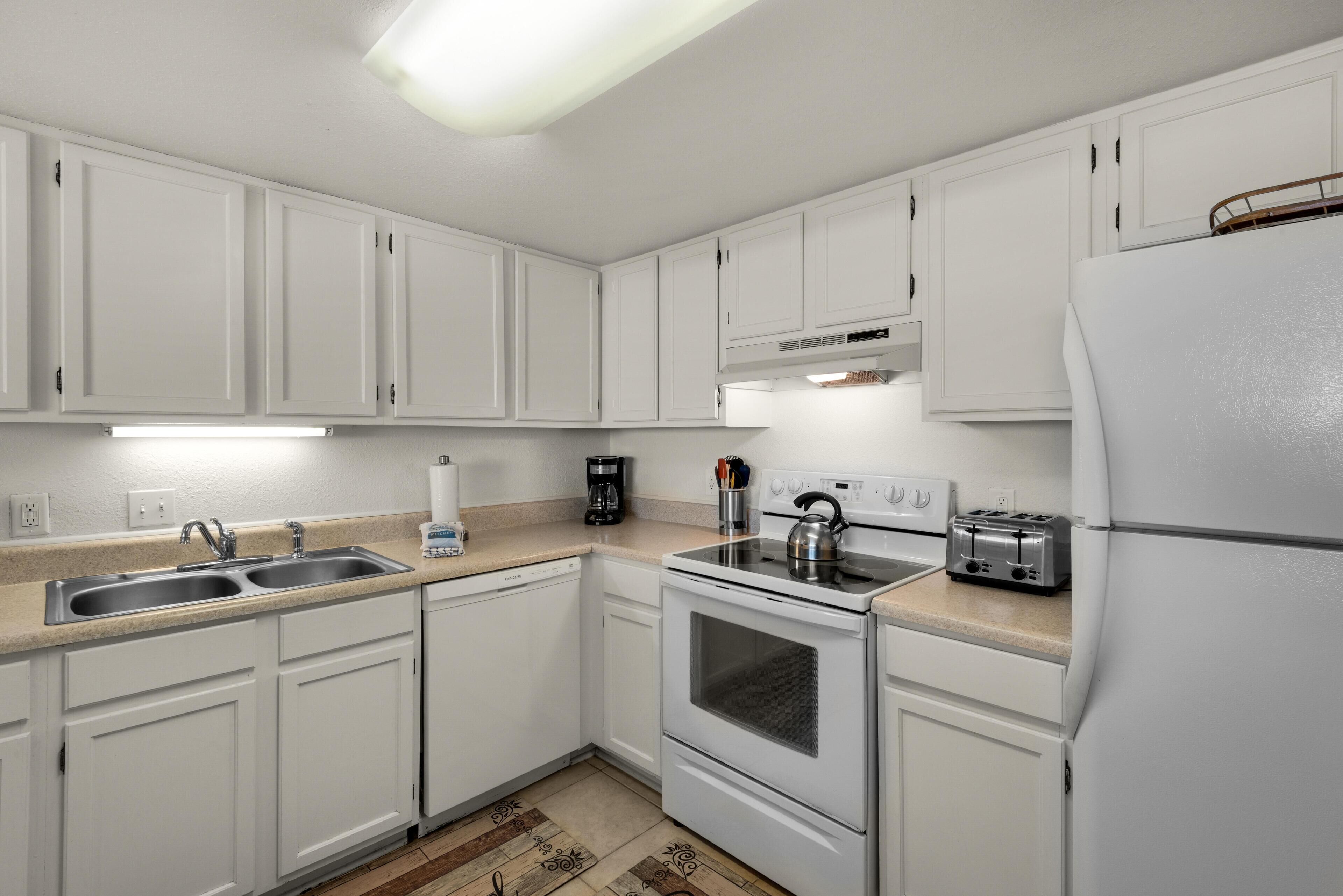 A modern kitchen with white cabinets, a double sink, a stove, and a refrigerator.