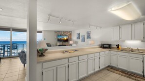 A modern kitchen with white cabinets, a large island, and a view of the ocean. - Starboard Village 423 (Pensacola Beach)