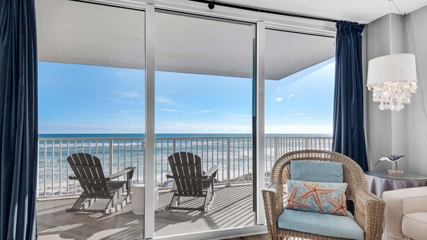 A balcony with two Adirondack chairs, a wicker sofa with a starfish pillow, and a view of the ocean. - Starboard Village 424- Beach Haven (Pensacola Beach)