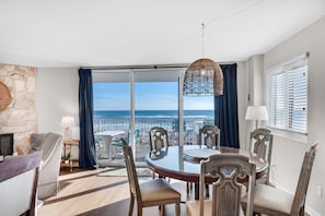 Un coin repas avec une table et des chaises en verre, une vue sur la plage et un mur en pierre.