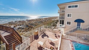 A beachfront property with a wooden deck, outdoor seating, and a swimming pool. - Starboard Village 424- Beach Haven (Pensacola Beach)