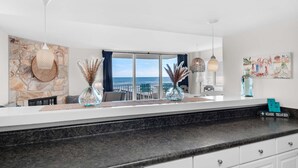 A modern kitchen with a stone backsplash, large windows, and a view of the sea. - Starboard Village 424- Beach Haven (Pensacola Beach)