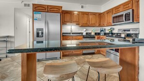A modern kitchen with wooden cabinets, a stainless steel refrigerator, a microwave, and a granite countertop. - Starboard Village 411 (Pensacola Beach)