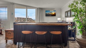 A modern kitchen with a large island, bar stools, a view of the sea, and a potted plant. - Starboard Village 411 (Pensacola Beach)