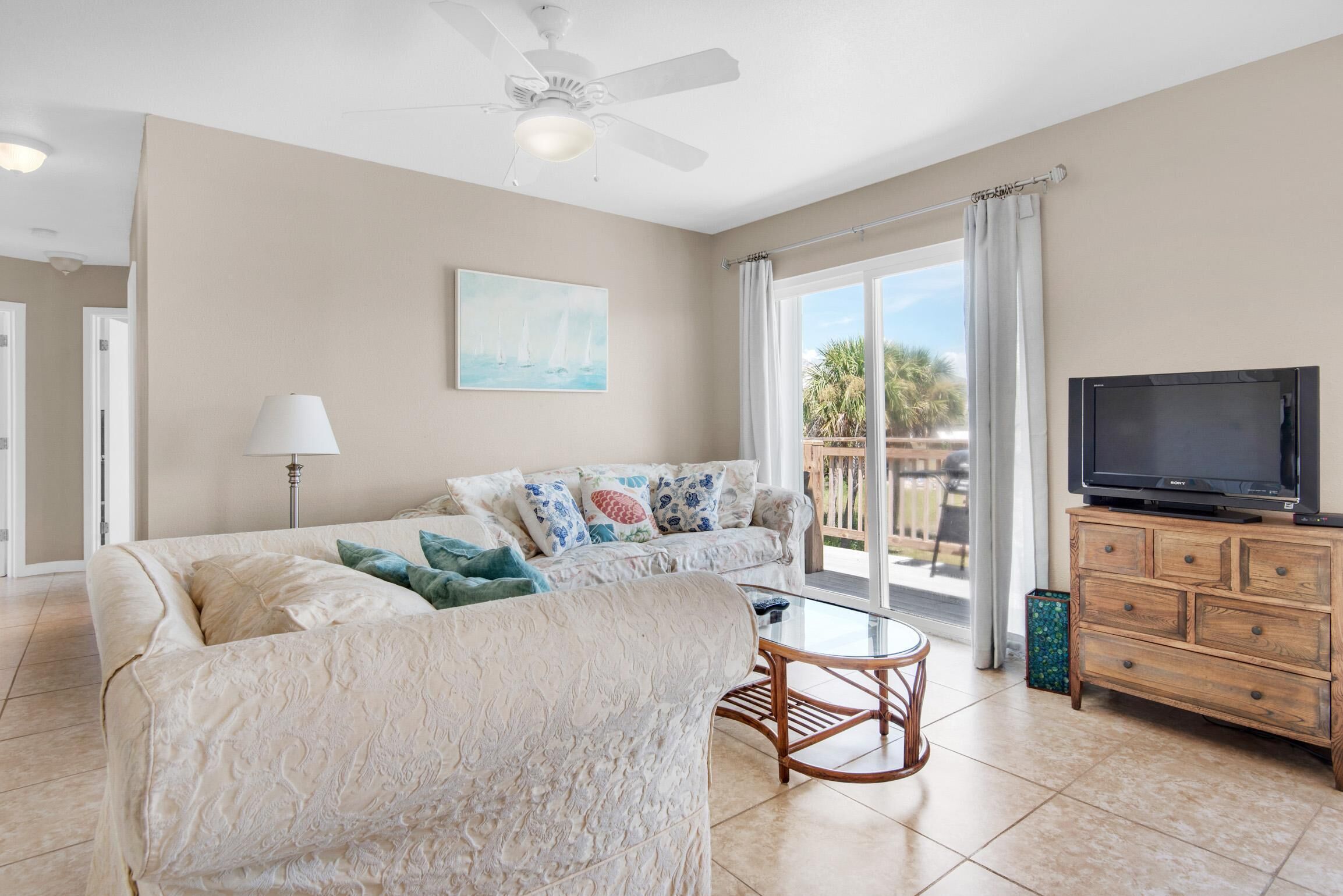 A living room with a sofa, a coffee table, a television, and a ceiling fan.