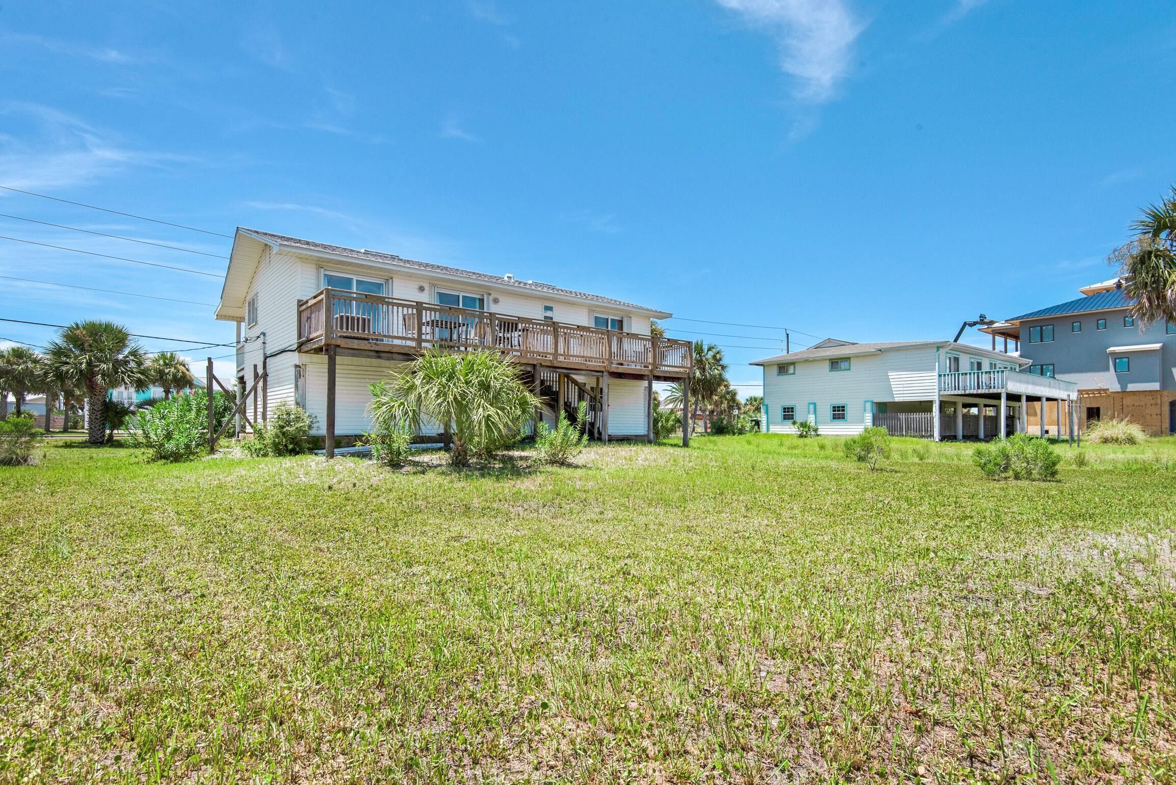 A two-story house with a balcony, surrounded by a grassy lawn and palm trees.