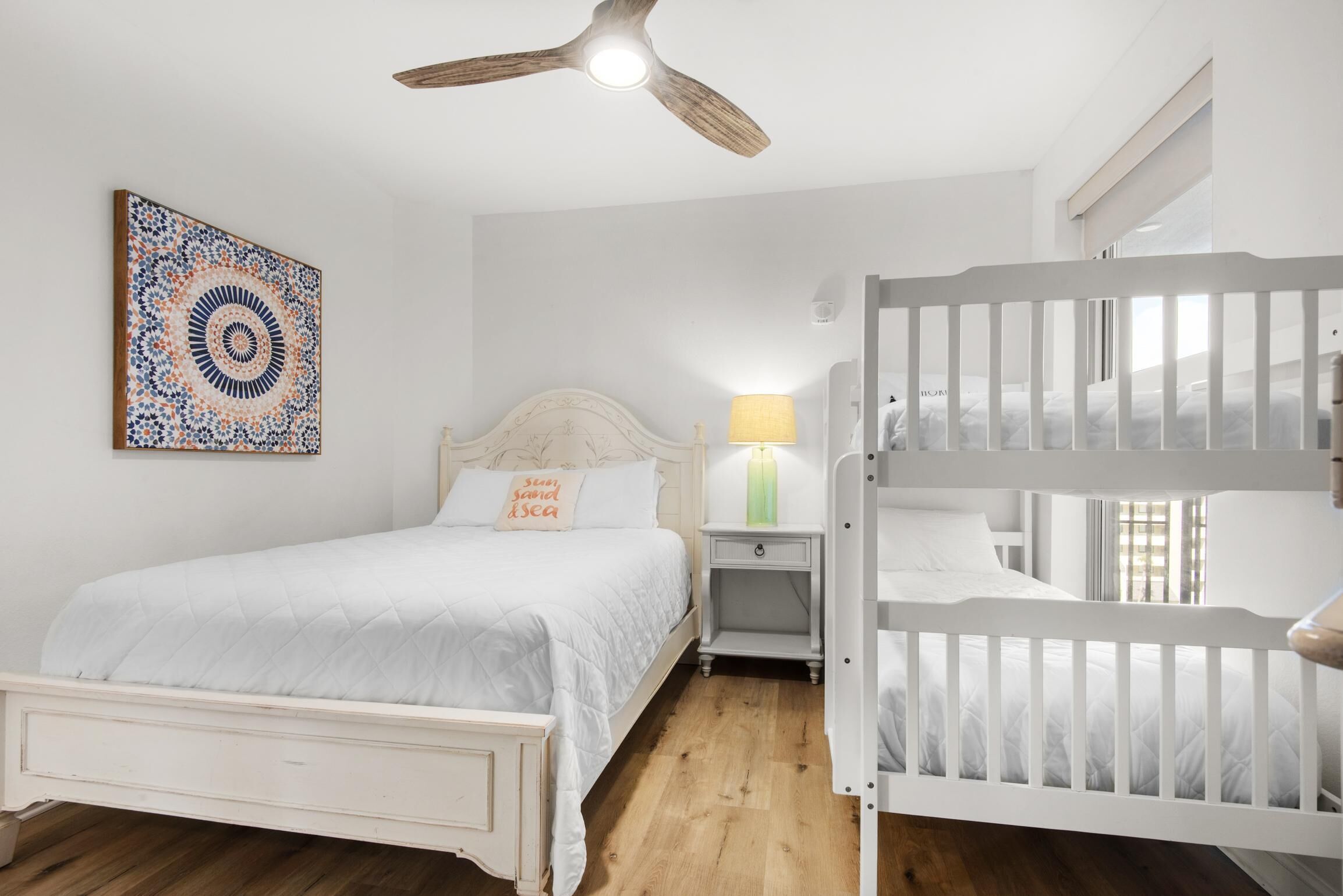 Ein Schlafzimmer mit einem Bett, einem Nachttisch, einer Lampe, einem Deckenventilator und einem Etagenbett.