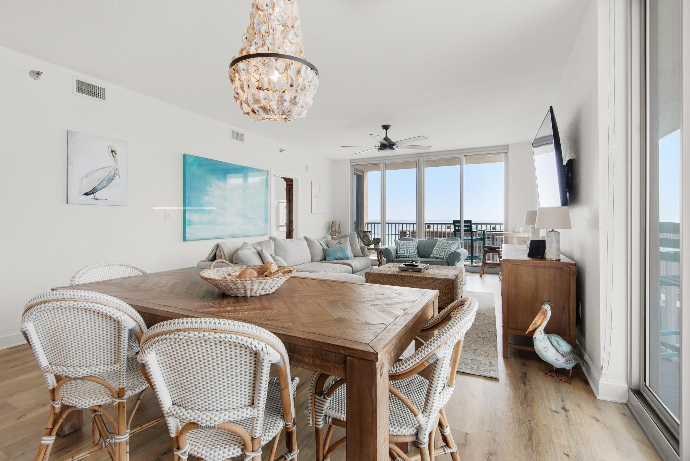 A spacious living area with a wooden dining table, wicker chairs, a large painting, and a view of the outdoors.