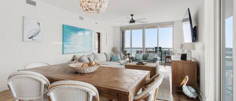 A spacious living area with a wooden dining table, wicker chairs, a large painting, and a view of the outdoors.
