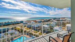A balcony with a view of a beach and ocean, a pool, and several buildings with blue roofs. - Tristan Towers Unit 9B (Pensacola Beach)