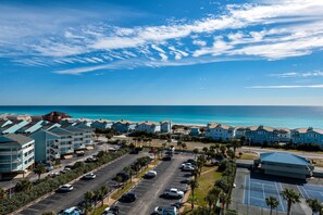 A coastal hotel with multiple-story buildings, a parking lot, and a view of the ocean.
