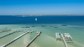 A marina with multiple docks and boats, clear blue water, and a distant shoreline. - Tristan Towers Unit 9B (Pensacola Beach)