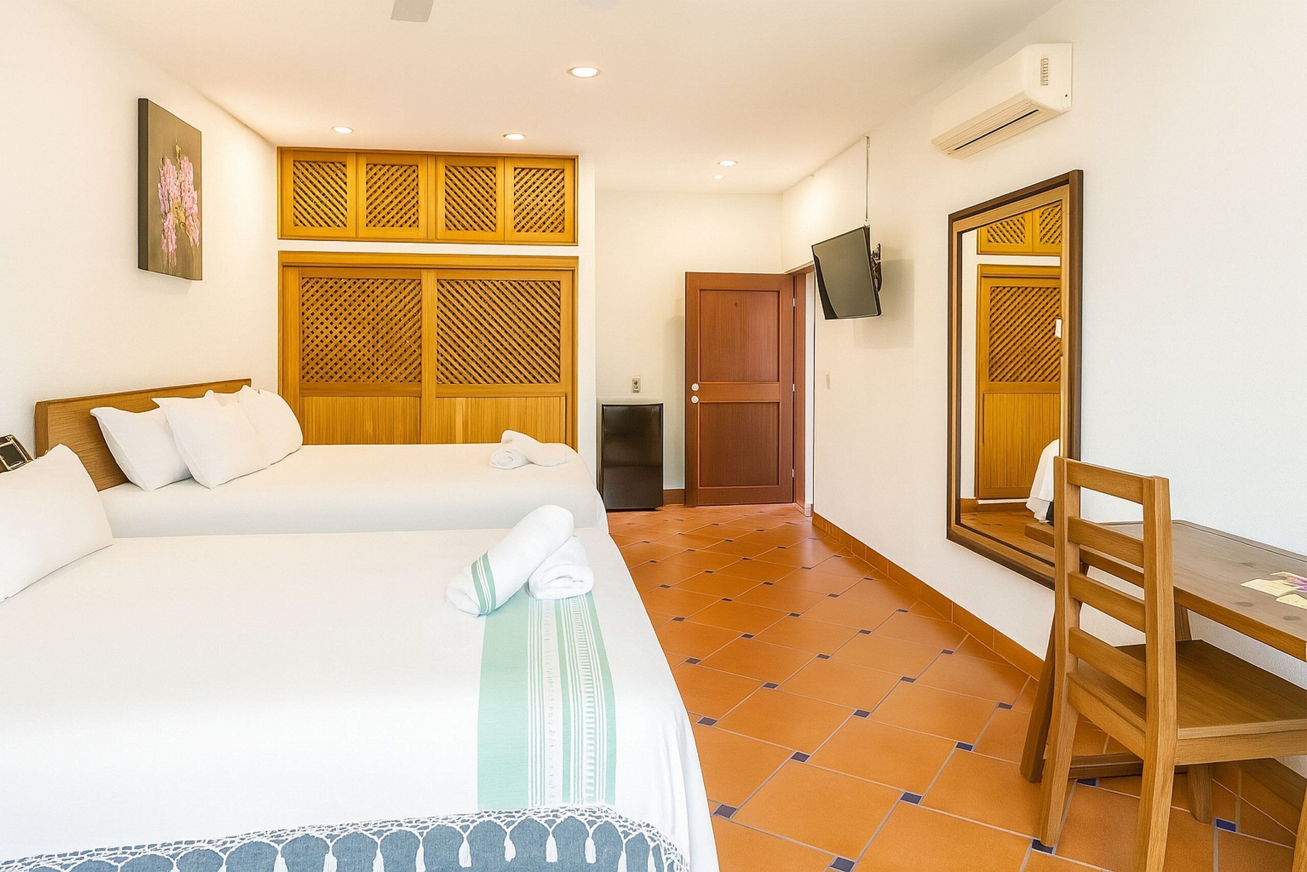 A hotel room with two beds, a wooden wardrobe, a TV, and a desk with a chair.