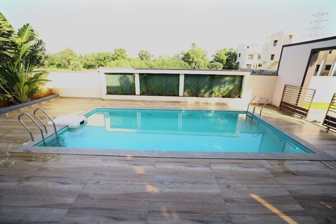 Una piscina rettangolare con bordo in legno, circondata da un muro bianco e una recinzione metallica.