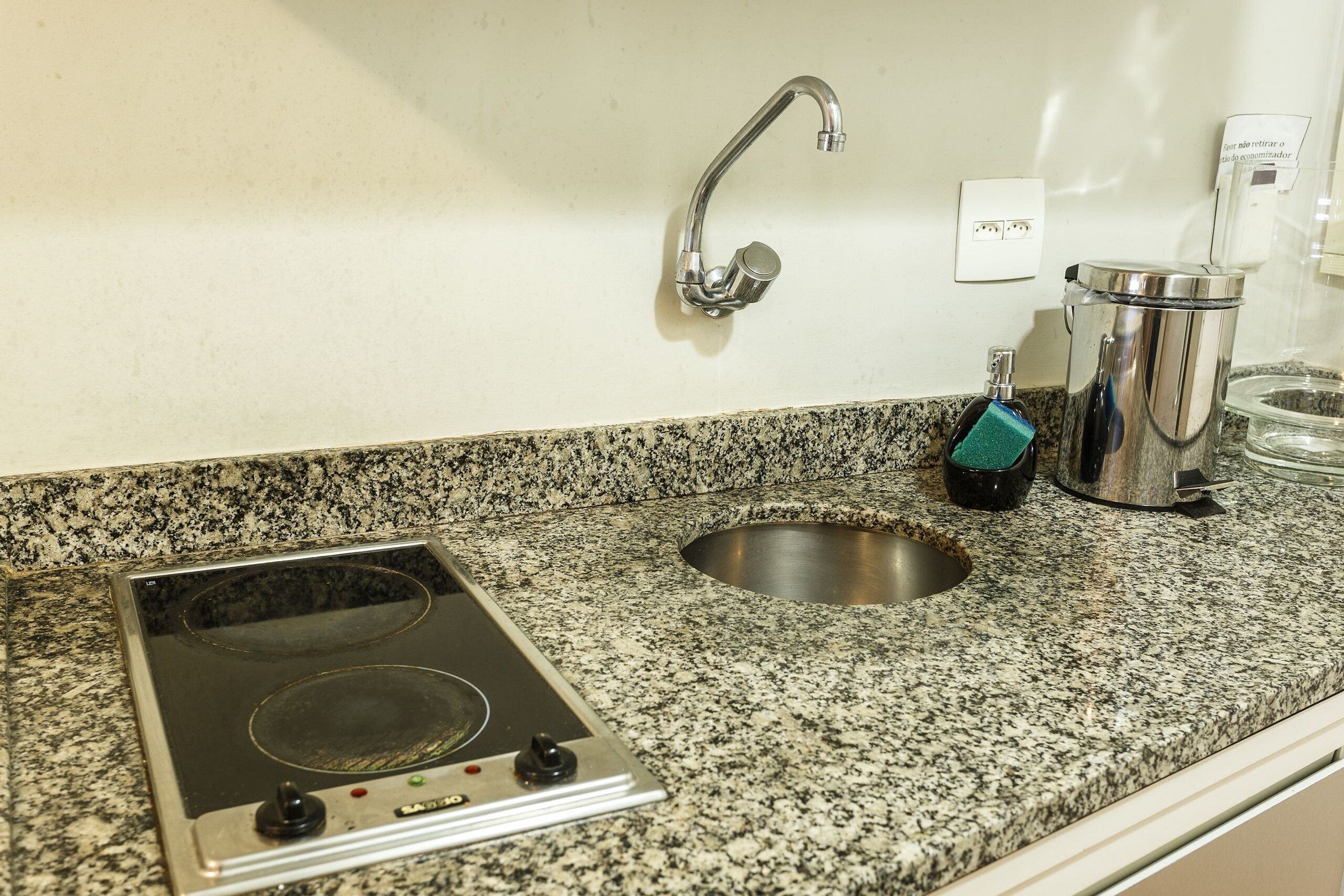 A kitchen with a granite countertop, a stainless steel sink, a built-in electric stove, a faucet, and a coffee maker.