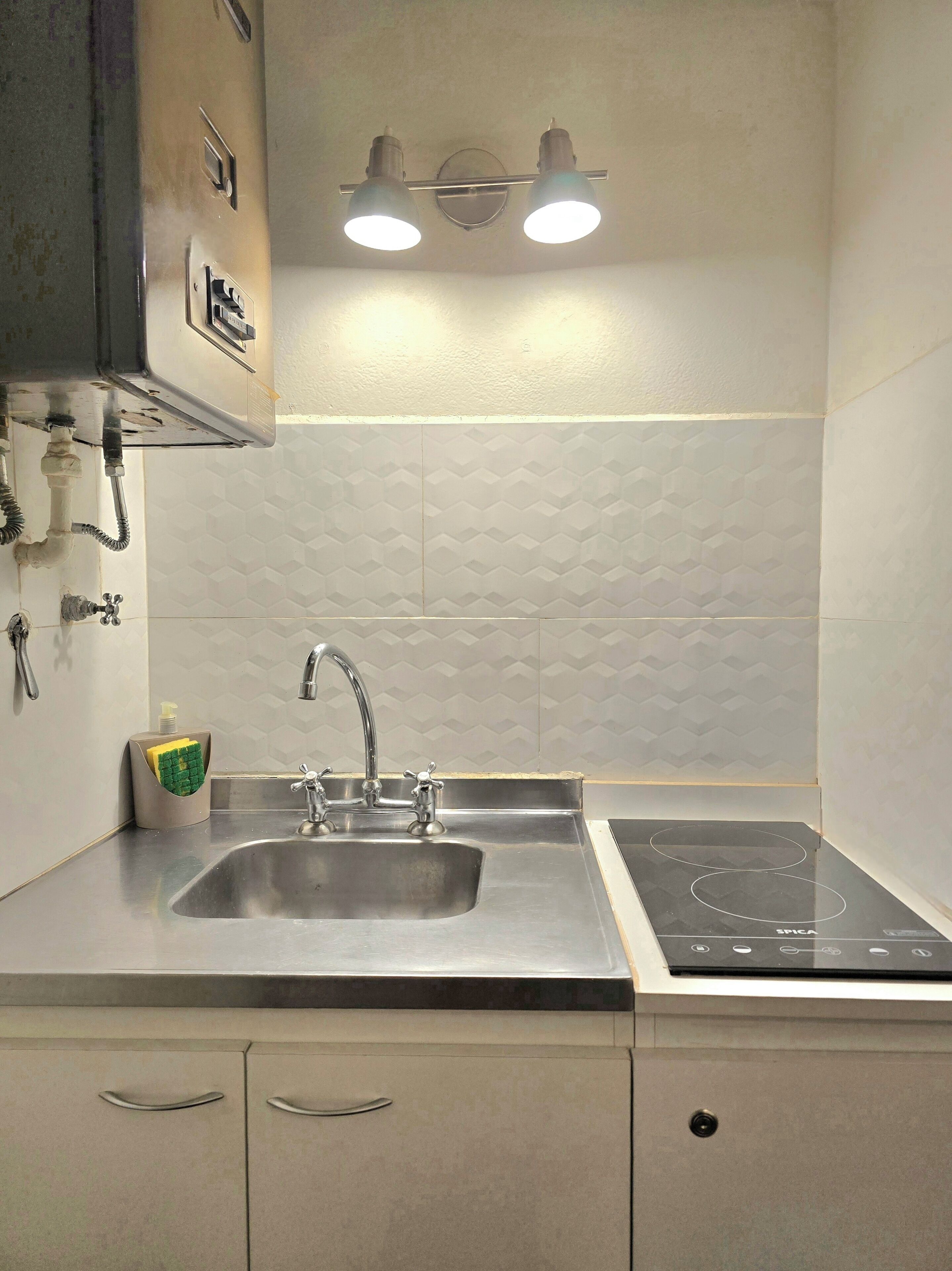 Una cocina con un lavamanos de acero inoxidable, una estufa eléctrica empotrada y un accesorio de luz montado en la pared.