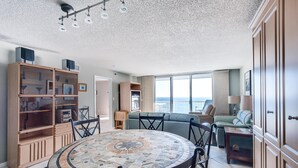 Ein großzügiger Wohnbereich mit einem runden Mosaik-Tisch, einer eingebauten Bücherwand, einer Couch und Blick aufs Meer.