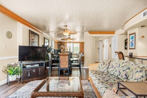 A living room with a television, sofa, and dining area. - Tristan Towers Unit 1B (Pensacola Beach)