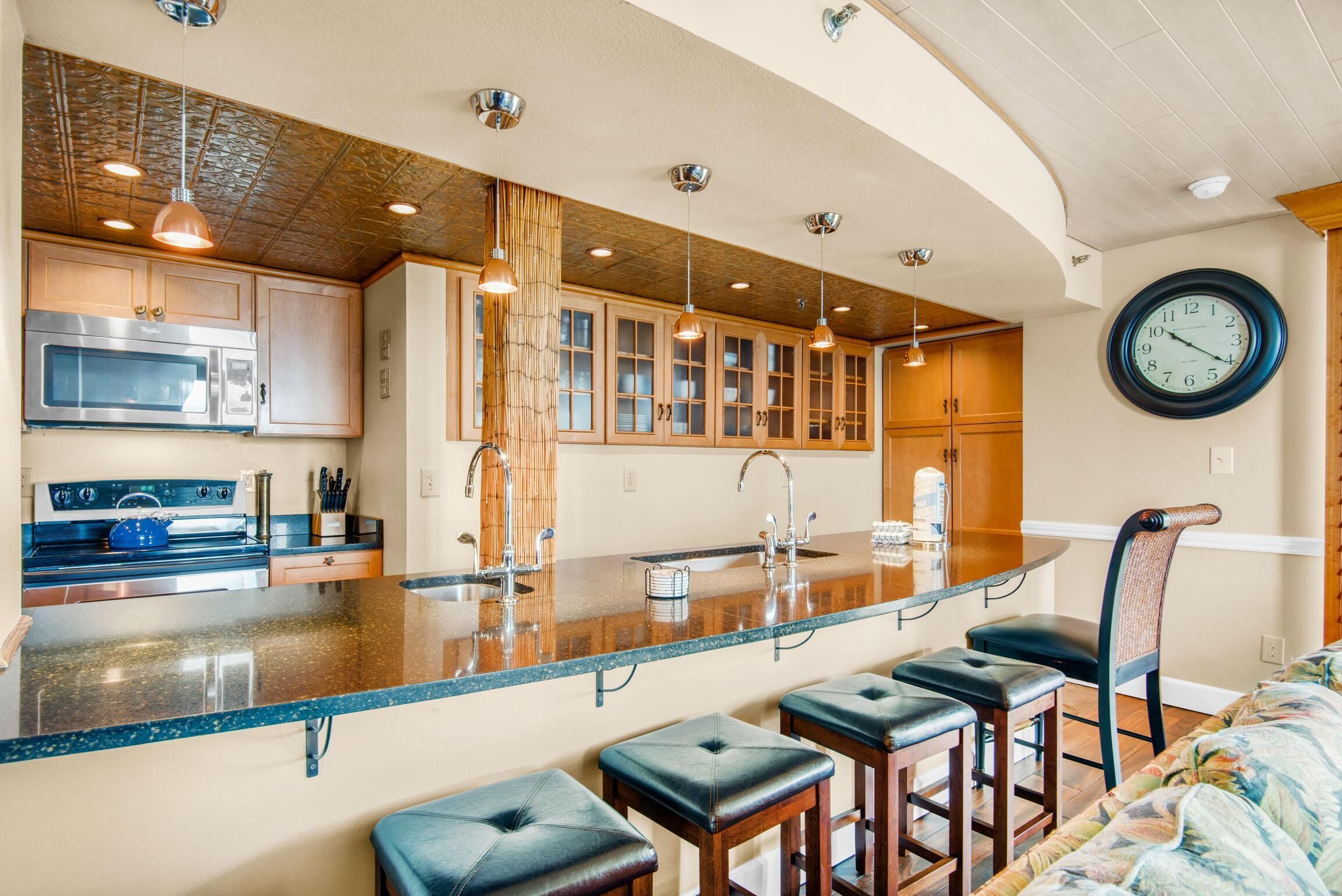 A kitchen with wooden cabinets, a stainless steel microwave, and a large island with bar stools.